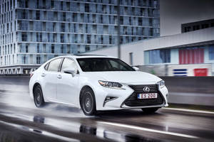 白色Lexus ES 200轎車在潮濕的城市街道上快速行駛，背景模糊。