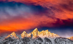 白雪覆蓋的山脈在火紅的天空下沐浴在金色的日落光中。 — 美麗的日落動畫 壁紙