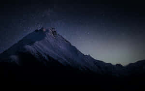 繁星夜空下帶有微弱極光輝光的雪山峰。 — 暮光 壁紙