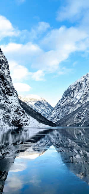 白雪覆蓋的山峰在冰凍的湖面上倒映，天空湛藍，白雲朵朵。 — Huawei 壁紙