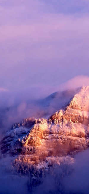 積雪的山峰在日出光芒中閃耀，位於雲霧之上。 — iPhone 14 Pro Max 壁紙