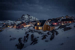 積雪的村莊房屋，夜晚溫暖的燈光在黑暗的山脈背景下閃耀。 — MacBook Air M3 壁紙
