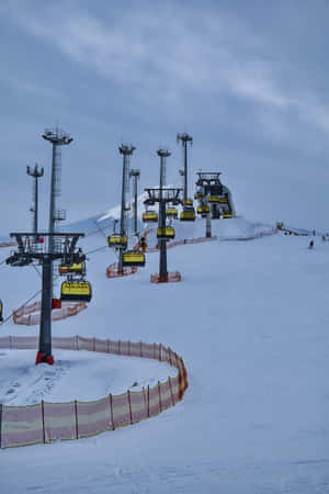 黃色滑雪纜車在陰天下沿著白雪覆蓋的山坡上升。 — 小米Mix 壁紙