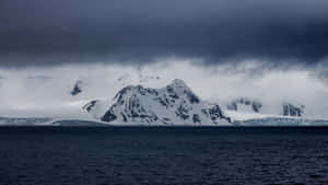 積雪的山峰從黑暗的海洋中升起，上方是暴風雲。 — 北極 壁紙