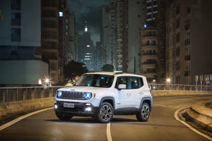 白色Jeep Renegade在夜間行駛於濕漉漉的城市街道上，建築物燈火通明。