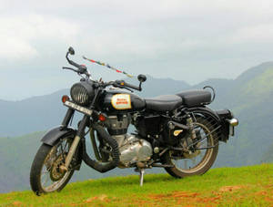 經典的 Royal Enfield 電單車停泊在長滿草的山丘上，以群山為背景。 — 皇室 壁紙