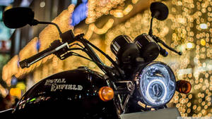 黑色Royal Enfield電單車，頭燈在夜間金色散景燈光中發光。 — 皇室 壁紙
