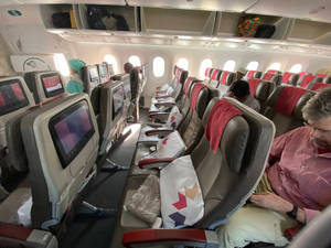 乘客坐在飛機機艙內，配有個人屏幕和頭頂行李架。 — 旅行 壁紙