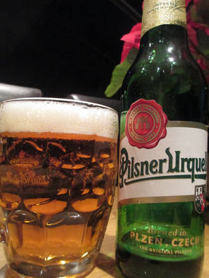 Pilsner Urquell啤酒瓶和玻璃杯在昏暗的燈光下放在木桌上。