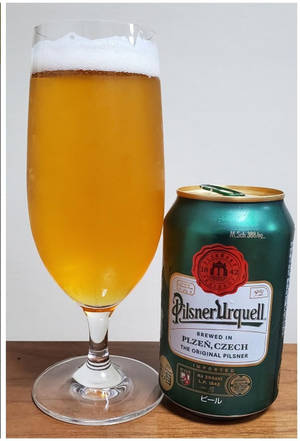 一杯啤酒放在木質表面上，旁邊有一個 Pilsner Urquell 罐。