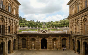 宏偉的石頭庭院，帶有拱形步道和雕像，通向一個綠色花園。 — 建築 壁紙