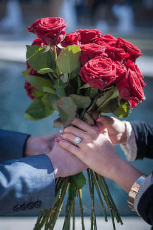 兩隻手緊握一束紅玫瑰，可見結婚戒指。