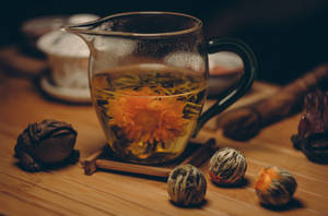 玻璃壺中盛開的菊花茶，木桌上放有青蛙公仔和茶球。
