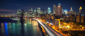 紐約天際線的夜景，建築物燈火通明，橋上車輛留下光跡。 — 1080x2400 壁紙