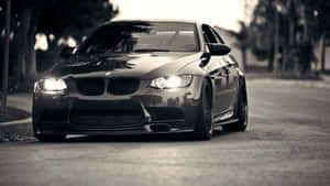 黑色BMW M3跑車開著車頭燈停放在有樹木的街道上。