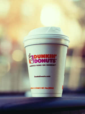 一個Dunkin' Donuts咖啡杯放在深色表面上，背景溫暖模糊。