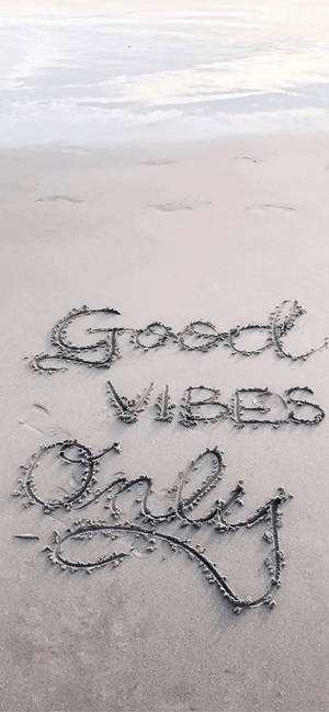 Good Vibes Only 以草書寫喺沙灘嘅濕沙上，海浪靠近。