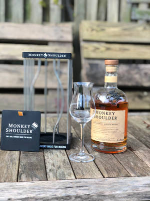 Monkey Shoulder威士忌瓶和品酒杯在戶外木桌上。