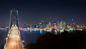夜間城市景觀，包括燈火通明的灣區大橋和舊金山天際線，水面上的光跡。
