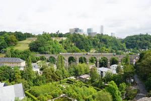 火車在石拱橋上，下方是綠色花園，背景是城市天際線。