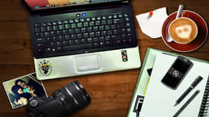 一張木製書桌，上面有筆記型電腦、相機、手機、咖啡杯和照片。