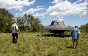兩個男人在多雲的天空下檢查草地上的大型UFO模型。