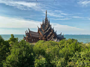 一座木製寺廟被綠樹環繞，背景是海洋和天空。 — 藍天 壁紙