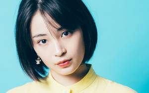 短黑髮、身穿黃色襯衫的年輕女性，藍色背景 — 日本 壁紙