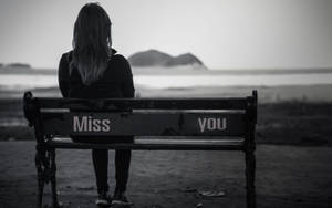 一個人獨自坐在海邊的長椅上，上面寫著「Miss you」。 — 傷心 壁紙