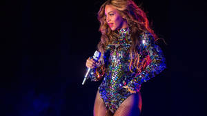 Beyonce 在舞台上穿著閃閃發光的緊身衣，手持麥克風唱歌