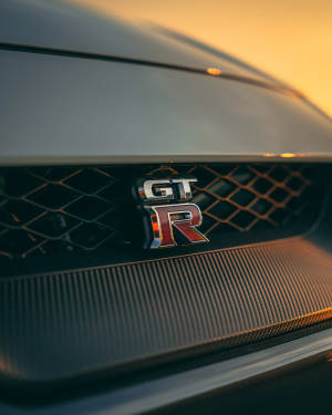 碳纖維格柵上GT-R汽車徽章沐浴在金色夕陽光中。 — 汽車 壁紙