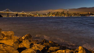 從岩石海岸觀看三藩市天際線和海灣大橋的夜景。
