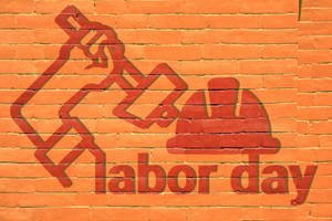 橙色磚牆上的紅色labor day塗鴉，帶有錘子和安全帽符號。