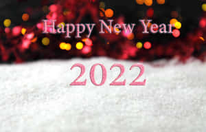 雪地上寫著「Happy New Year 2022」的粉紅色閃光文字，帶有模糊的節日燈光。