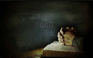 雙手合十祈禱，放在打開的聖經上，裂縫牆壁上有「have FAITH in GOD」的文字。 — 神 壁紙