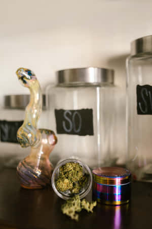 罐子裡的大麻花蕾、研磨器和玻璃水煙槍在木架上。