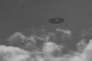 在粗糙的黑白圖像中，飛碟盤旋在烏雲之上。