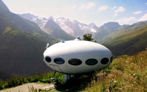 白色UFO形狀小屋位於山脊上，背後有白雪覆蓋的山峰。