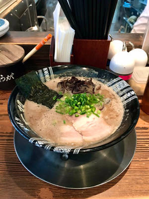 一碗熱騰騰的拉麵，有豬肉、青蔥和海苔，放在木桌上。