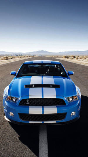 藍色 Shelby Mustang 帶白色條紋，在沙漠公路日落時分。 — 藍色 iPhone 壁紙