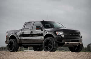 黑色福特F-150 Raptor pickup貨車喺碎石上，背景係陰天天空。