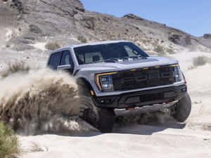 銀色福特 Raptor 卡車在沙漠沙地中行駛，揚起灰塵。