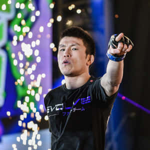 一位穿著黑色襯衫的武術家在明亮的舞台燈光下向前指。 — 運動 壁紙