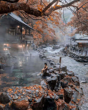 一位女士浸泡在溫泉中，周圍是秋葉和木建築。 — 秋天 壁紙