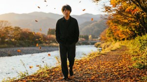 男子在河邊秋葉小徑上行走，夕陽