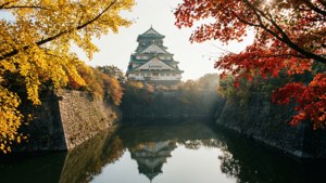 一座歷史悠久的日本城堡倒映在平靜的水面上，周圍環繞著色彩繽紛的秋樹。