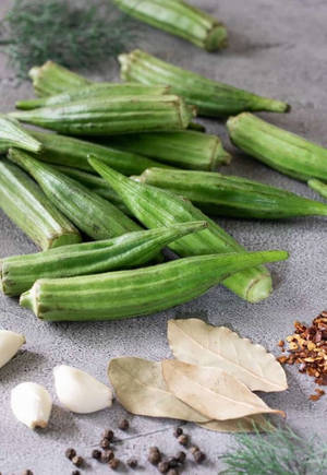 灰色表面上的新鮮秋葵、大蒜、月桂葉、黑胡椒粒和紅辣椒片