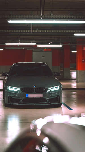 一輛深灰色BMW跑車停在一個光線昏暗、有紅色柱子的地下車庫中。 — 9:16 壁紙