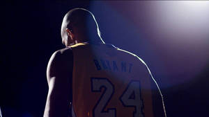 籃球運動員Kobe Bryant身穿黃色球衣24號，在聚光燈下的背面視角。