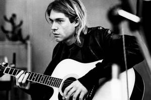 Kurt Cobain 在陰鬱的室內環境中彈奏木結他。